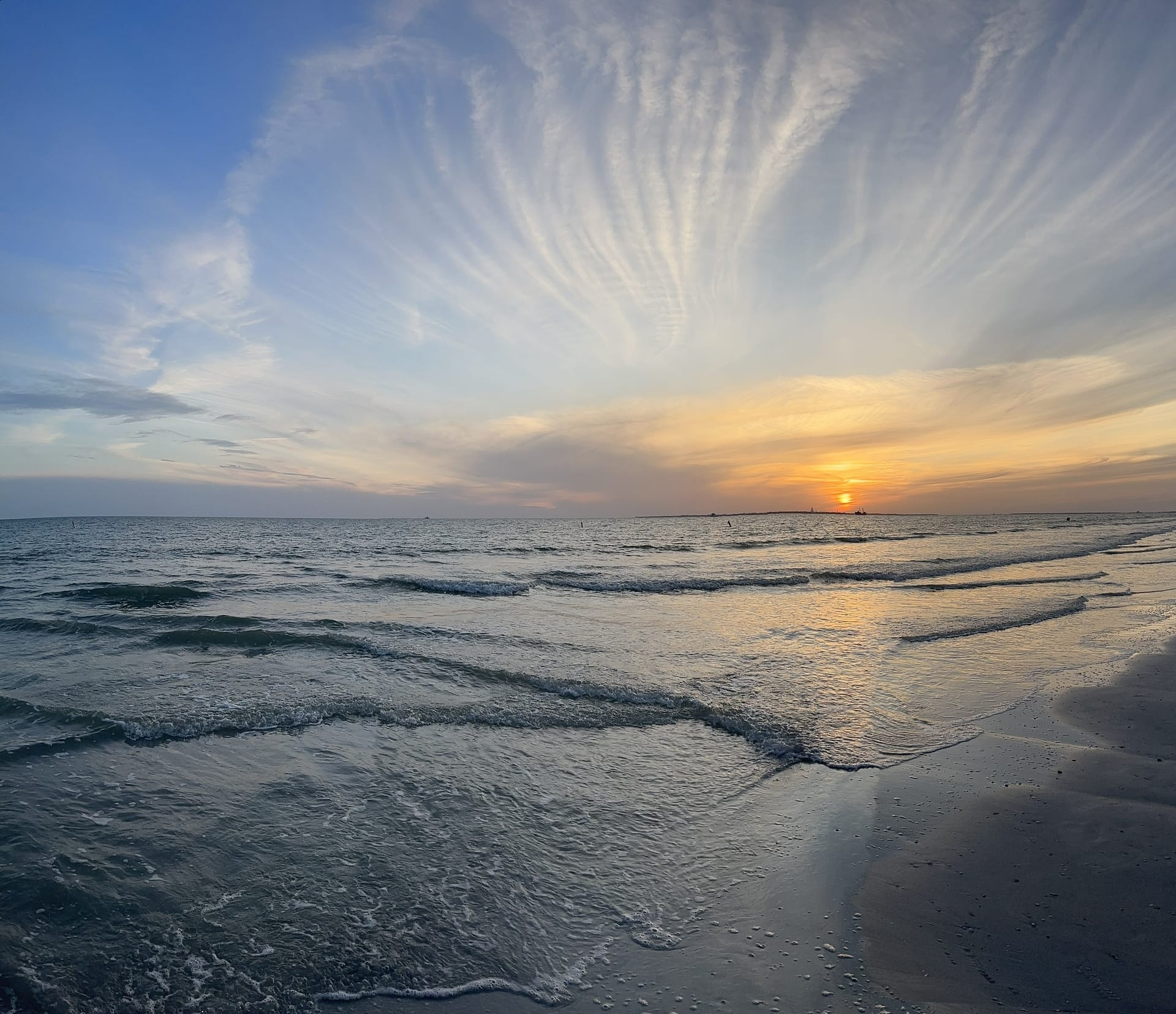 A soft sunset over quiet waves, wispy clouds fanning across the sky